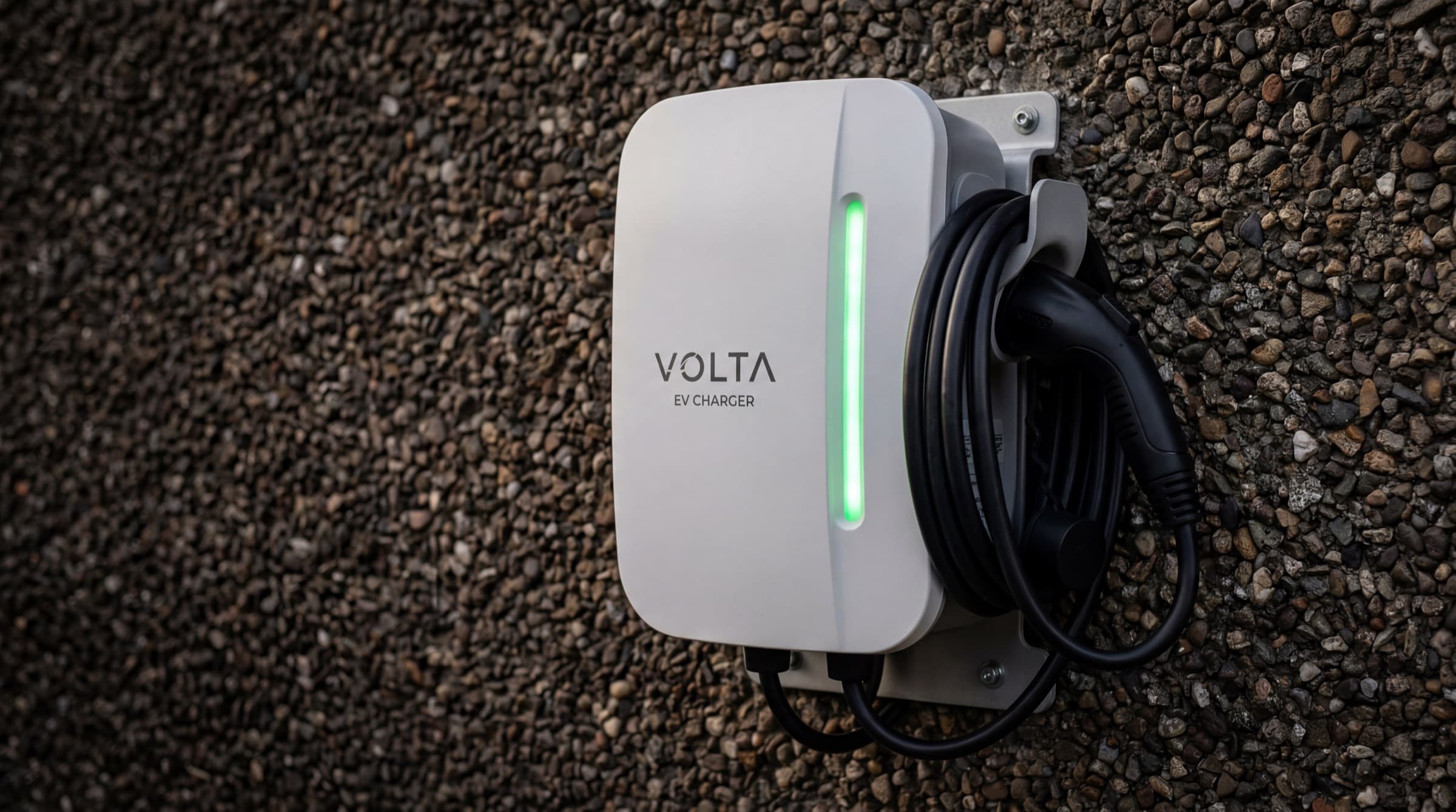 Close-up product shot of a premium white wall-mounted EV charger on an Irish pebble-dash render wall with green LED strip glowing